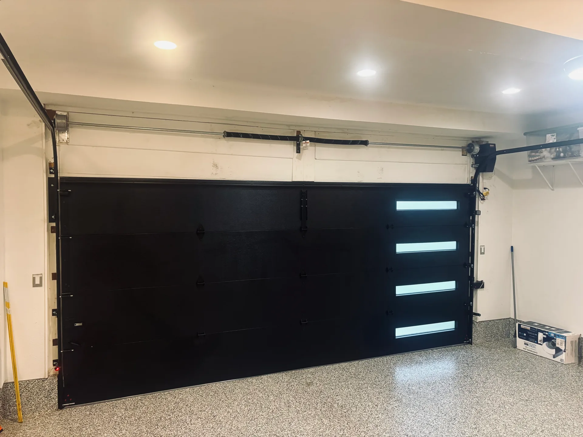 Black flush-panel garage door with vertical window lites installed by DNA Garage Doors